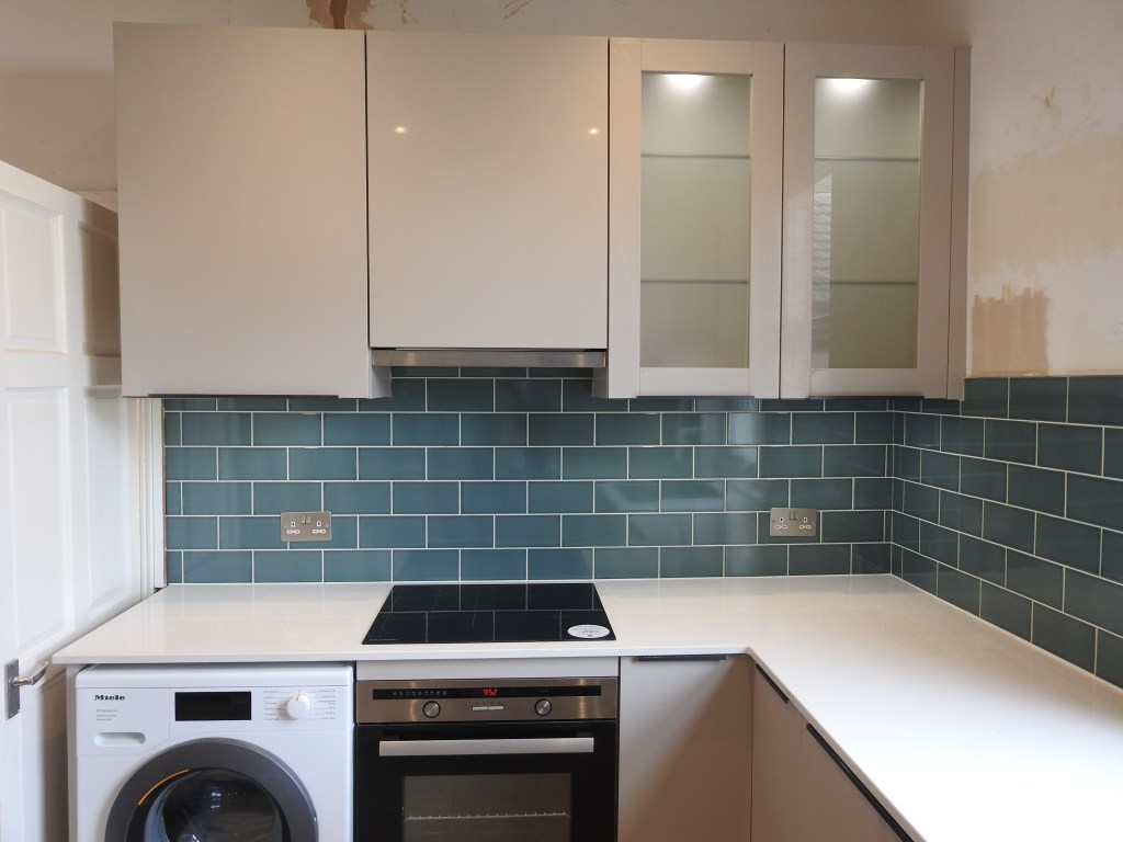 A view of part of a kitchen with the cupboards on show and the metro tiles underneath them before the white marble work surface. You can see the top of a washing machine and cooker. 